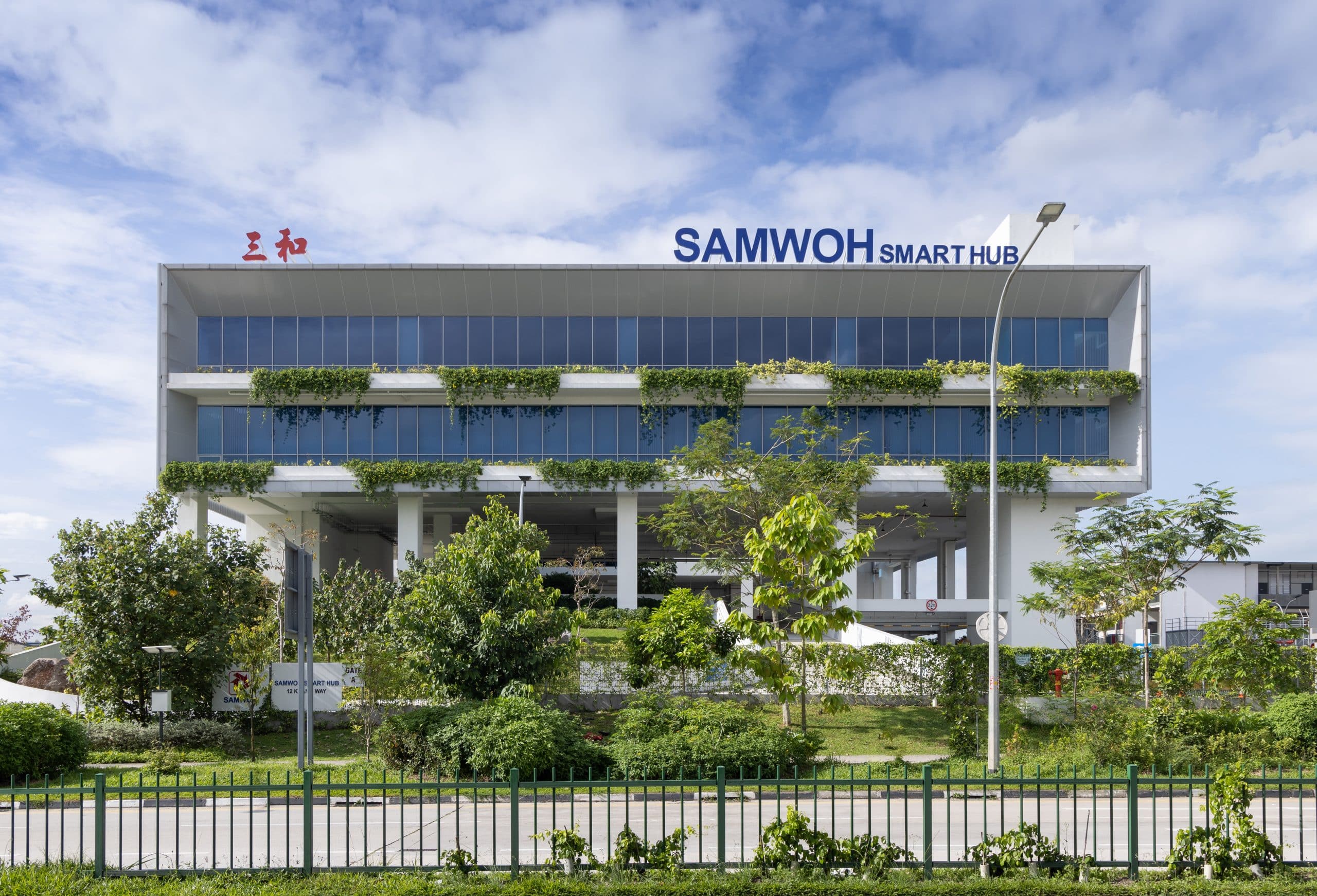 Full facade view of the Samwoh Smart Hub in Singapore, highlighting its contemporary design. Singapore's first positive energy industrial building boasts solar panels on the roof, expansive glass windows, and integrated greenery, reflecting its commitment to sustainability and innovation.